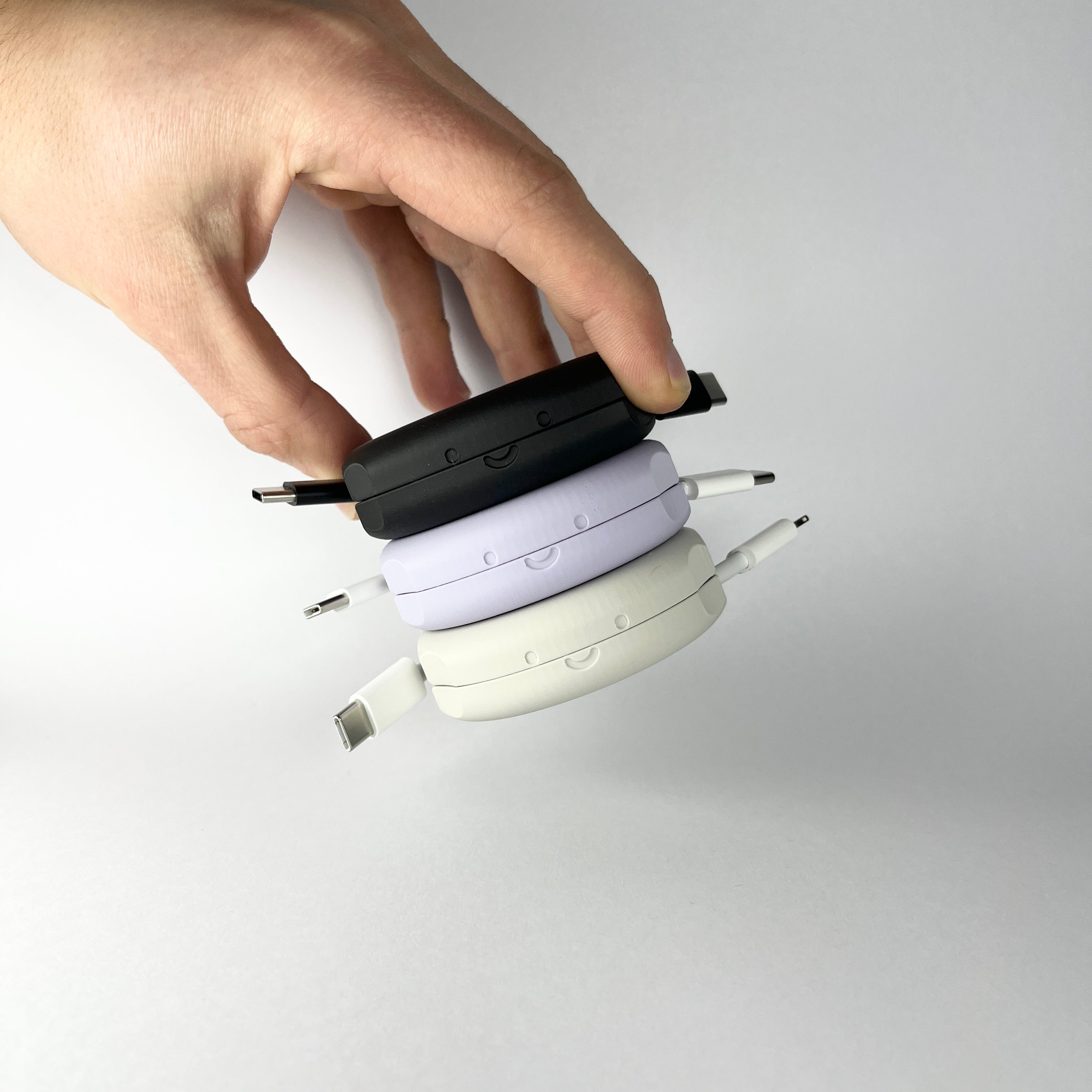 a person holding a black, purple and white pebbl 1 mini automatic cable organisers that are stacked magnetically 